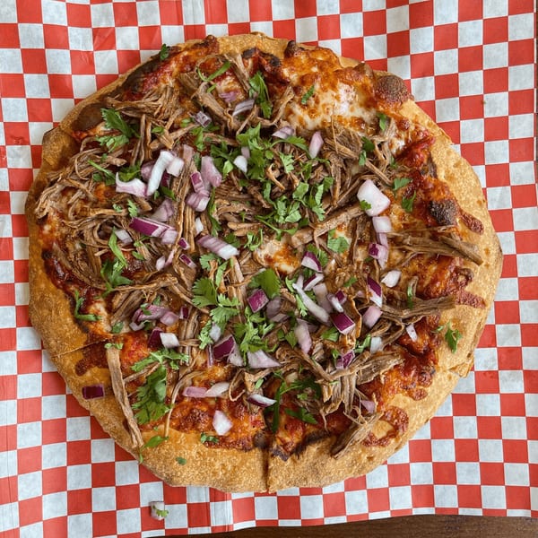Pizza Presidente's pizza topped with shredded meat, red onions, and cilantro on checkered paper.
