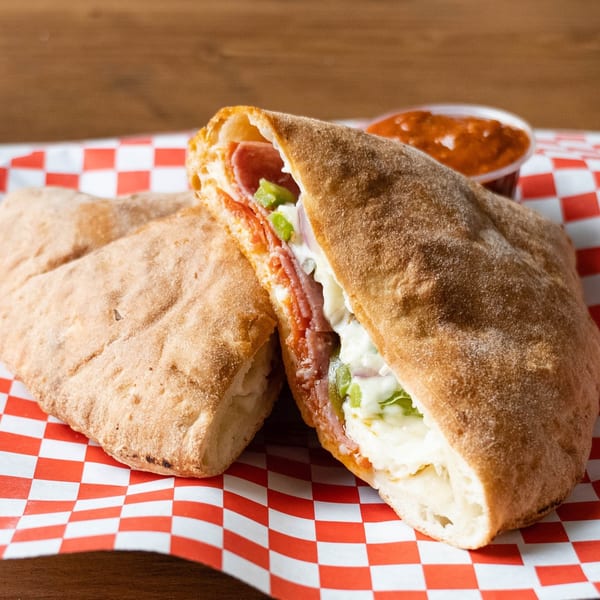 A calzone cut in half, revealing pepperoni, cheese, and green peppers, with a side of marinara.