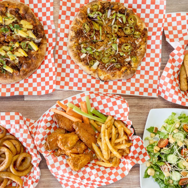 Two pizzas, chicken wings, fries, onion rings, and a salad on a wooden table.