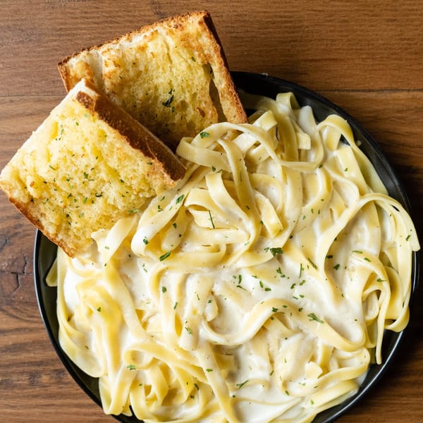 Creamy fettuccine alfredo pasta with two slices of garlic bread on a black plate.