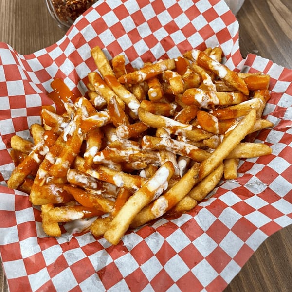 Golden french fries drizzled with red and white sauces, served in a red and white checkered paper basket.