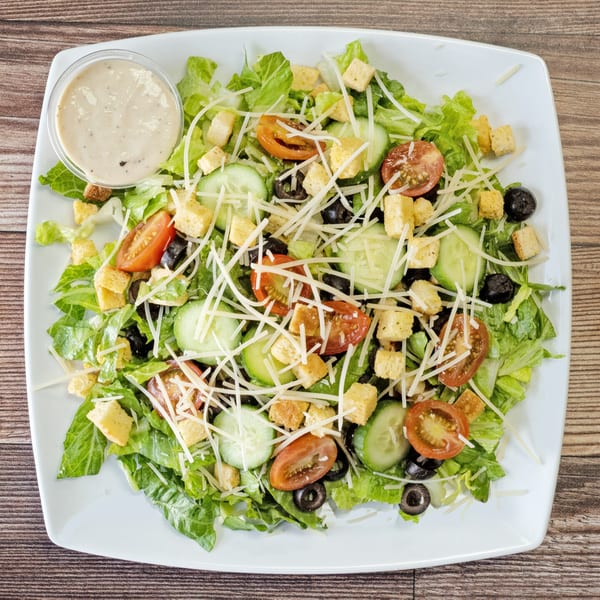 Fresh garden salad with lettuce, tomatoes, cucumbers, olives, croutons, shredded cheese, and dressing.