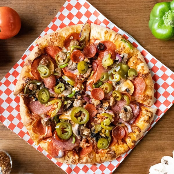 A whole Pizza Presidente pizza with pepperoni, sausage, mushrooms, olives, and jalapeños on a checkered paper.