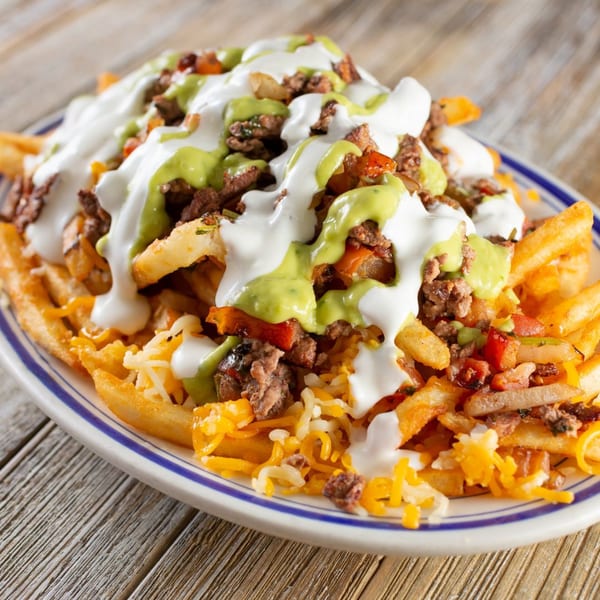 Loaded fries with ground meat, shredded cheese, white sauce, and green sauce on a plate.