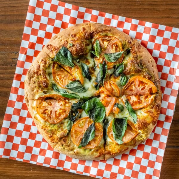 Pizza Presidente's Margherita pizza with fresh tomatoes and basil on checkered paper.