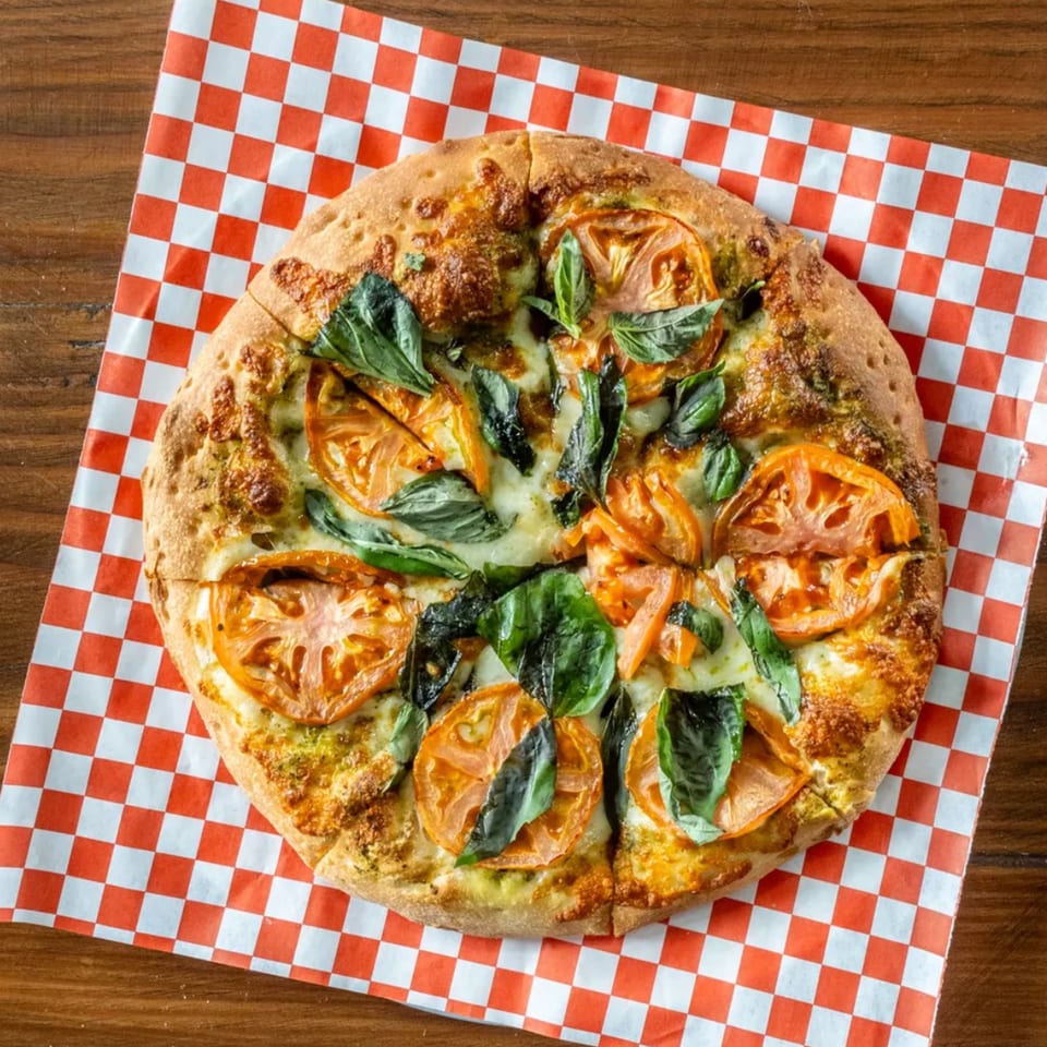 Pizza Presidente's Margherita pizza with fresh tomatoes and basil on checkered paper.