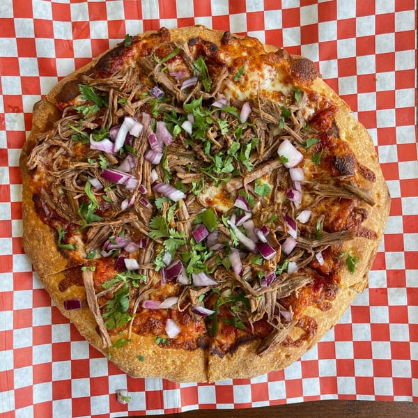 A Pizza Presidente pizza with shredded meat, red onions, and cilantro on red and white checkered paper.