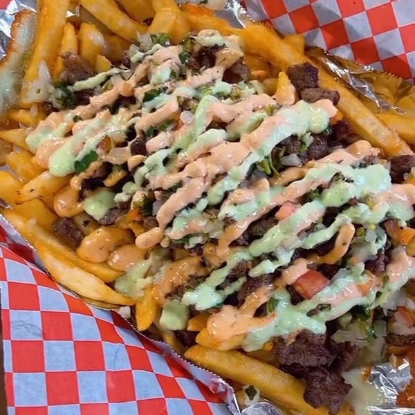 Golden french fries topped with steak, pico de gallo, and a drizzle of green and orange sauces.
