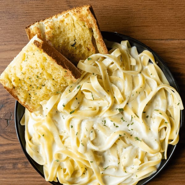 Creamy fettuccine alfredo pasta with two slices of garlic bread on a wooden table.